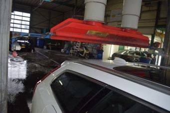 Binnenruimte autogarage met rood apparaat en witte cilinders boven witte auto, workshop autocosmetica groningen