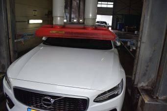 Wit volvo voertuig in werkplaats onder rood inspectie apparaat met verticale buizen - onderhoud auto Klein Autopoets Groningen