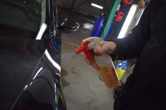Sprayfles met oranje vloeistof gebruikt voor autolak behandeling in garage auto-onderhoud detailing
