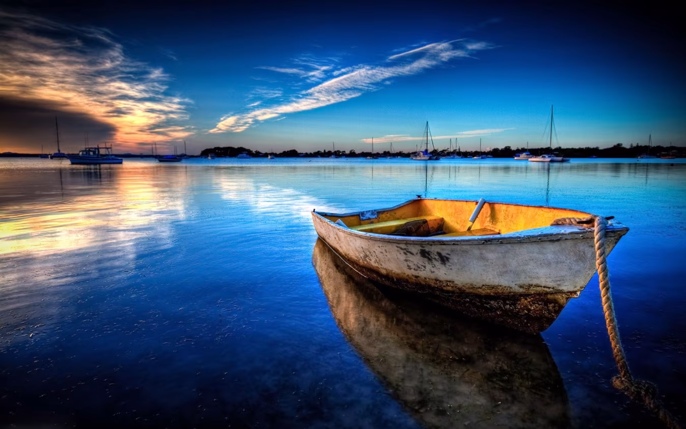 Boot op kalm water bij zonsondergang met reflecties en meerdere zeilboten op achtergrond rustige sfeer h2 boten & vaartuigen