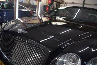 Fotograaf maakt foto van zwarte Bentley met prominent logo en radiatorrooster in garage omgeving klein autopoets groningen
