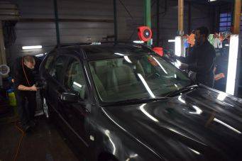 Autowerkplaats met zwarte auto en twee mensen in actie bij onderhoud en reparatie, autocosmetica groningen