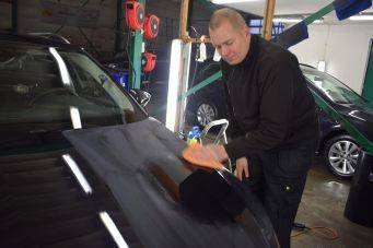 Autoreiniging en detailing in werkplaats met persoon die motorkap van zwarte auto poetst, oranje doek en autocosmetica