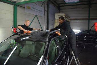 Binnenwerkplaats in Groningen met twee mensen die een zwarte auto met glazen dak reinigen - Klein Autopoets Groningen