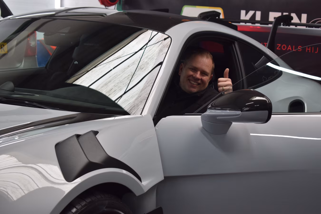 Ontmoet Frits Klein: grijze sportwagen met duim omhoog in showroom bij Klein Autopoets Groningen