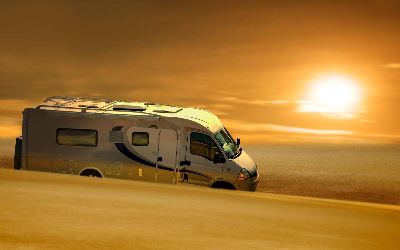 Camper in woestijn bij zonsondergang met warme geel-oranje lucht symboliseert avontuur en reizen