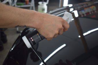 Autoverzorging in de werkplaats met schoonmaakproducten en een zwarte auto die wordt gepoetst aan de bestuurderszijde achter