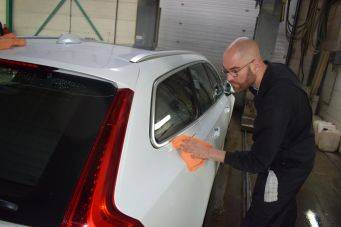 Binnenruimte met gesloten roldeur. Witte auto wordt schoongemaakt met oranje doek. Schoonmaak in garage. Klein Autopoets Groningen.