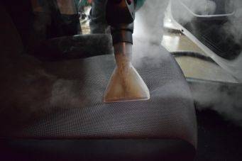 Close-up van een met zeep schuimende witte spons en groene handschoen die een auto wast in een garage