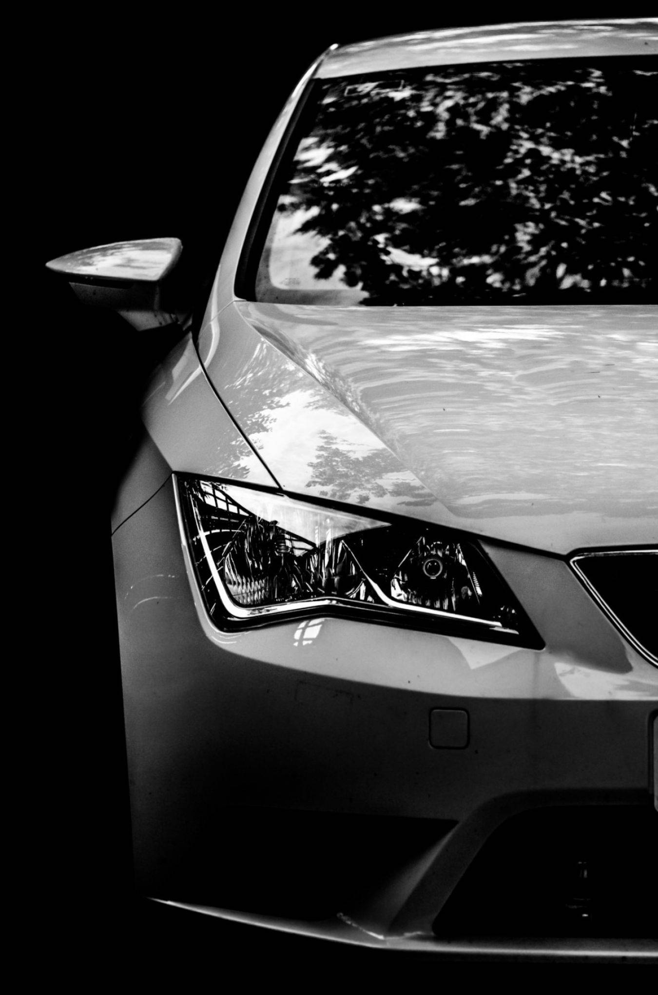 Close-up zwart-wit foto linker voorkant auto met scherpe koplamp en reflecties op motorkap alle autolakken