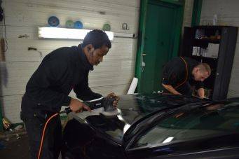 Autopolijsten in een garage met focus op zwarte auto en verlichtingsbalk, autoonderhoud proces