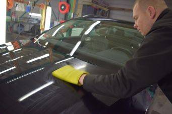 Binnenruimte autowerkplaats met Annemarie Jager die zwarte auto met gele doek polijst autocosmetica groningen