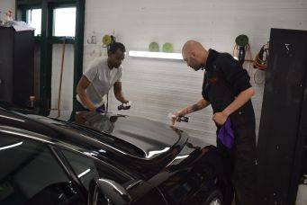 Autoverzorging in gloednieuwe werkplaats details glanzende zwarte auto polijsten professioneel team