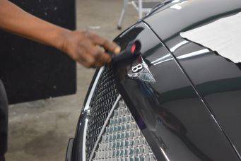 Close-up van bentley emblem en motorhuis bij auto-detailing met borstel glanzende zwarte lak klein autopoets groningen