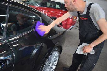 Iemand poetst zwarte auto met paarse doek in garage naast rode auto h2 autocosmetica groningen