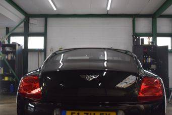 Zwarte luxe auto achterkant met rode achterlichten en gele kentekenplaat in garage Werkplaats