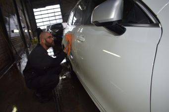 Binnenruimte autowerkplaats met witte auto en persoon die auto poetst met oranje doek - autocosmetica in Groningen