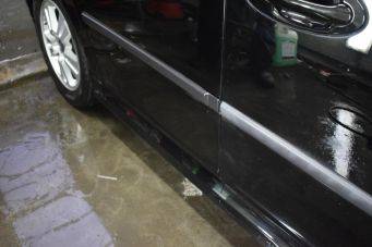 Zwarte auto onderkant portieren en lichtgekleurde velg op natte glanzende grond Reflectie carrosserie schoonmaak in Groningen