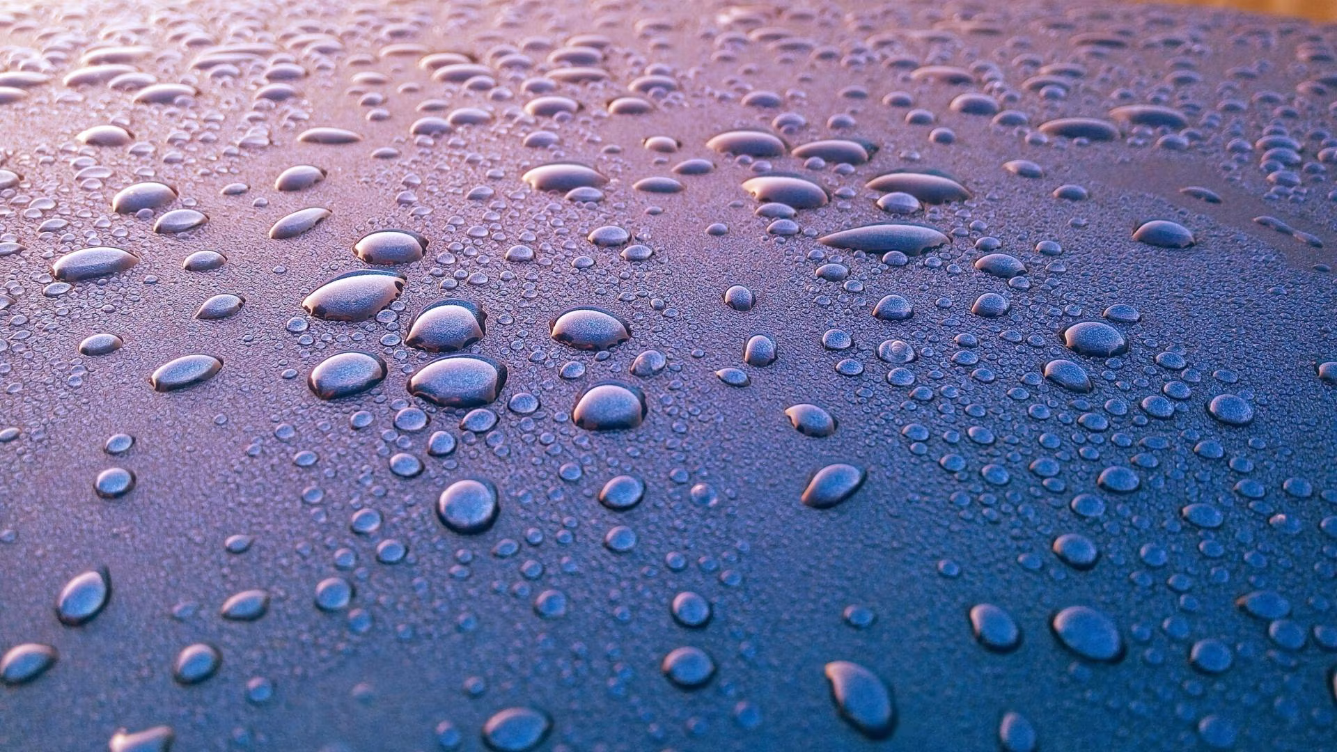 Close-up van waterdruppels op glanzend oppervlak met blauwe paarse tinten weerspiegelt licht in autopoets groningen