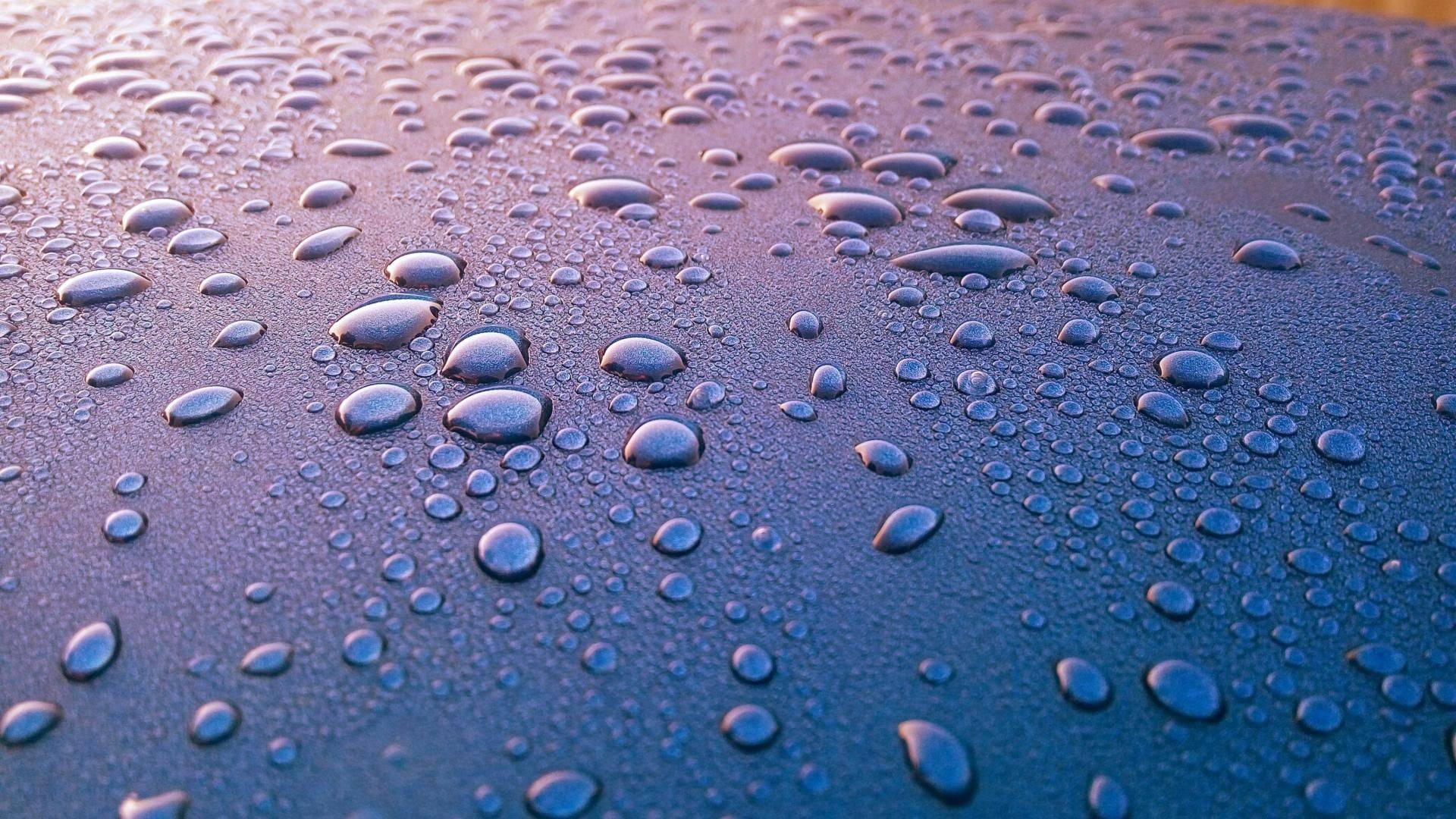 Close-up van waterdruppels op glanzend oppervlak met blauwe paarse tinten weerspiegelt licht in autopoets groningen