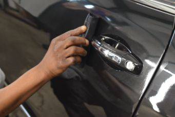 Detail van hand die zwarte autoportiergreep reinigt met klein zwart voorwerp glanzend oppervlak autoverzorging
