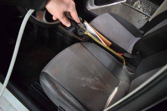 Interieur auto met focus op autostoel en hand die stoomreiniger gebruikt om vlekken te verwijderen