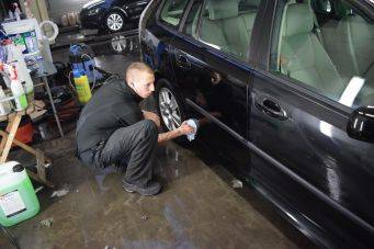 Activiteit in autowerkplaats met iemand die rechter achterdeur van zwarte auto poetst voor autoverzorging