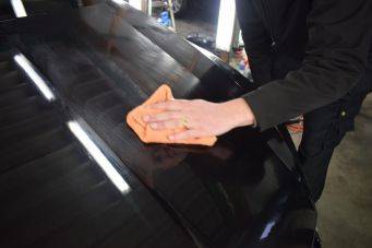 Close-up van glanzend donker voertuigoppervlak dat gepolijst wordt met oranje doek in autopoets werkplaats