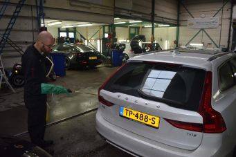 Binnenruimte autowerkplaats met witte Volvo T4 kenteken TP-488-S en schoonmaker met slang autopoets Groningen