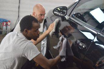 Twee mensen poetsen autopoets detailen zwarte auto zijkant onder spiegels in garage