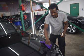 Werkruimte autopoetsen met persoon die zwarte auto polijst met paarse doek in garage met rode machines