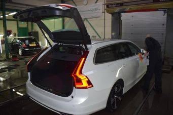 Binnenruimte garage met witte stationwagen met open achterklep en achterlichten aan, werkzaamheden aan rechterachterportier