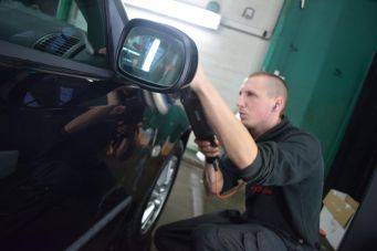 Reparatie auto met warmtepistool bij buitenspiegel in garage, autocosmetica Groningen, Klein Autopoets