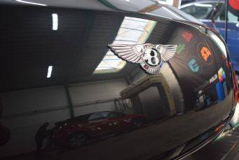 Close-up van chique bentley logo met vleugels op glanzend zwart oppervlak in showroom hoge kwaliteit autocosmetica