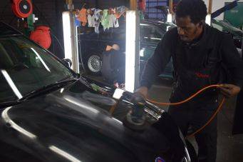 Garage werkplaats auto onderhoud focus op polijsten motorkap elektrisch polijstapparaat oranje kabel autocosmetica