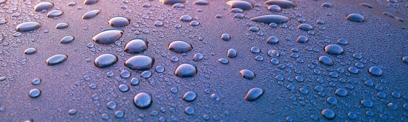 Close-up waterdruppels op glad oppervlak met reflecties in paarse en blauwe tinten, thema protector